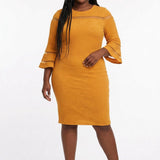 Plus-size model wears a mustard yellow textured sheath dress with sheer stripe detail, 3/4 bell sleeves, and crew neck;