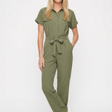 Blonde female model wearing an olive green short-sleeve belted jumpsuit with collar, chest pockets, and wide-leg pants;
