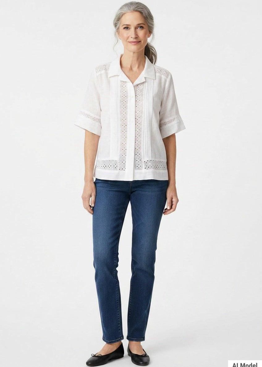 White short-sleeve button-front blouse with eyelet insets and pintuck detail, worn by a woman with gray hair, front view.