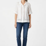 White short-sleeve button-front blouse with eyelet insets and pintuck detail, worn by a woman with gray hair, front view.