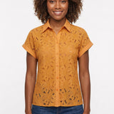 Woman wearing a golden orange short-sleeve eyelet button-front blouse with collar and cuffed sleeves, paired with dark
