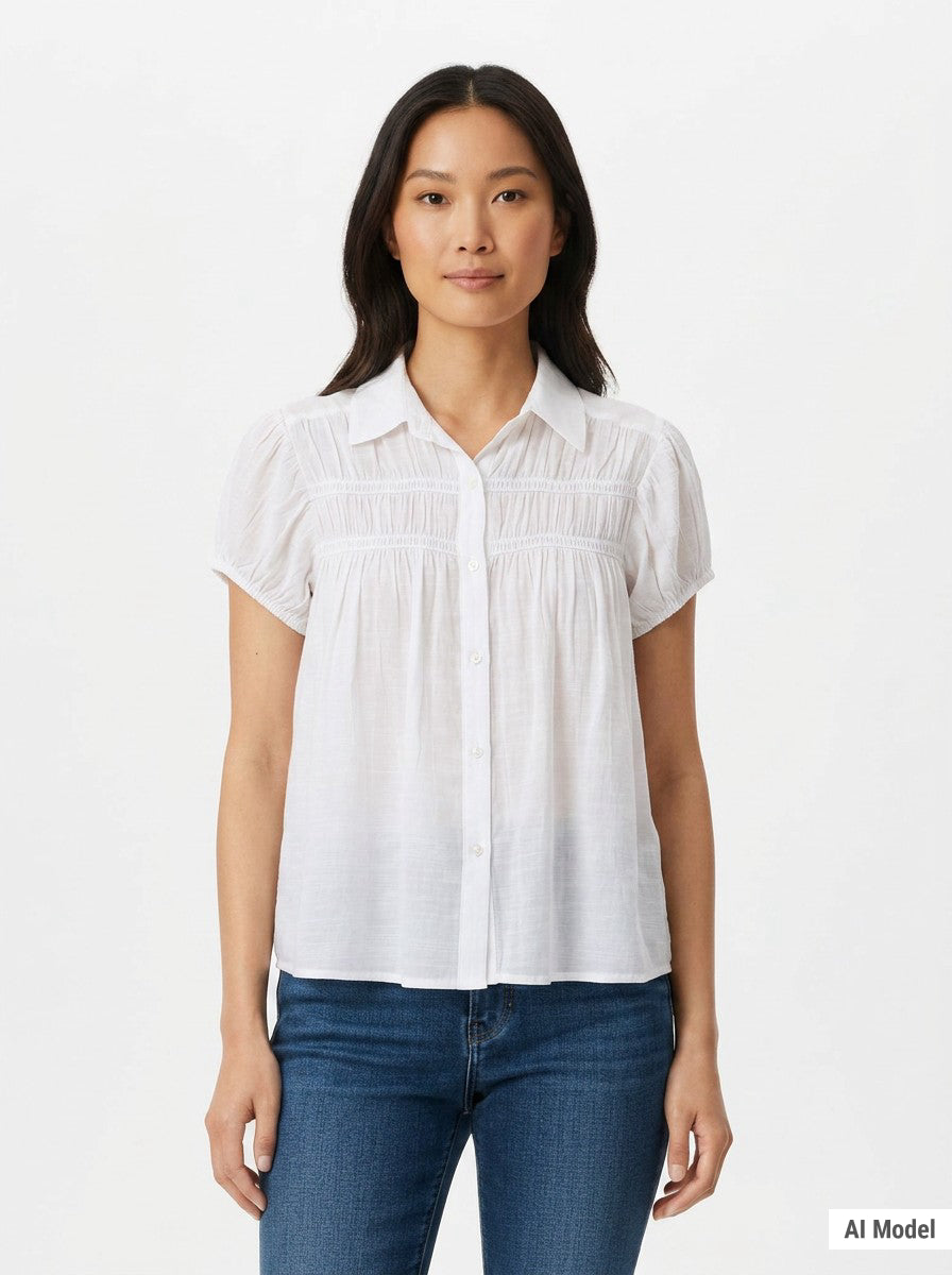 Woman wearing a white short-sleeve button-front blouse with ruched yoke detail and puff cap sleeves, paired with blue jeans;