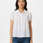 Woman wearing a white short-sleeve button-front blouse with ruched yoke detail and puff cap sleeves, paired with blue jeans;