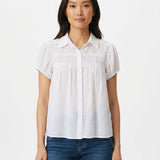Woman wearing a white short-sleeve button-front blouse with ruched yoke detail and puff cap sleeves, paired with blue jeans;
