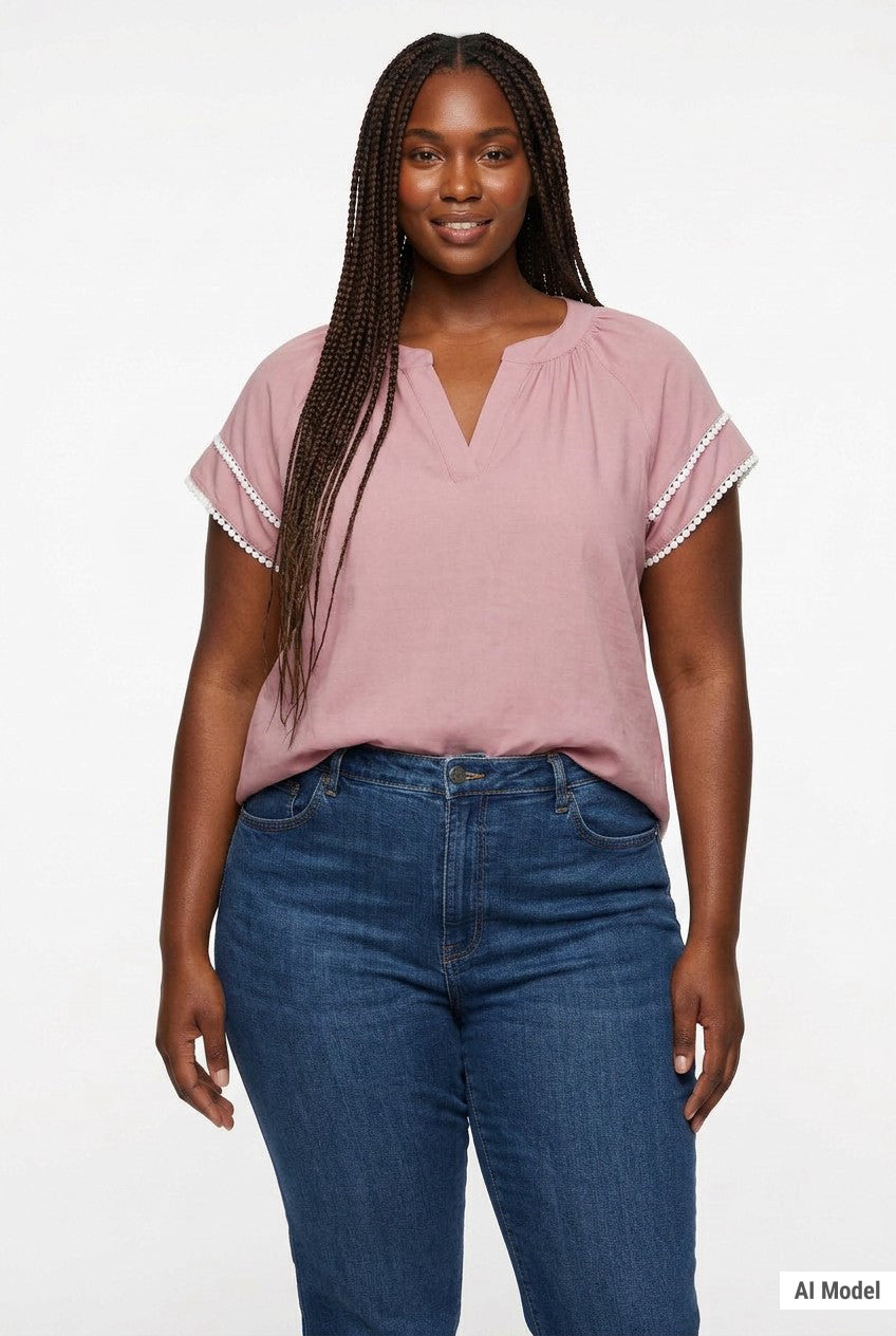 Plus-size model wears a dusty pink V-neck popover blouse with white lace-trimmed flutter sleeves, paired with blue jeans,