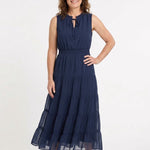 Navy sleeveless swiss dot maxi dress with tie ruffle neckline, smocked waist, and tiered skirt on a woman, front view.