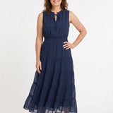 Navy sleeveless swiss dot maxi dress with tie ruffle neckline, smocked waist, and tiered skirt on a woman, front view.