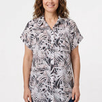 Woman wearing a short rolled-sleeve button-front blouse in black, white, and pink palm leaf print, with a collar and chest