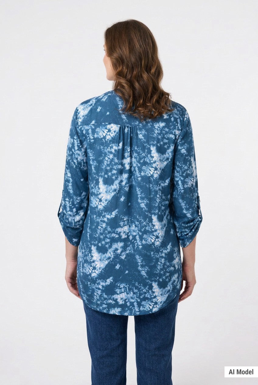 Back view of a woman wearing a blue and white tie-dye print tunic top with roll-tab 3/4 sleeves and curved hem, paired with