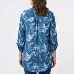 Back view of a woman wearing a blue and white tie-dye print tunic top with roll-tab 3/4 sleeves and curved hem, paired with