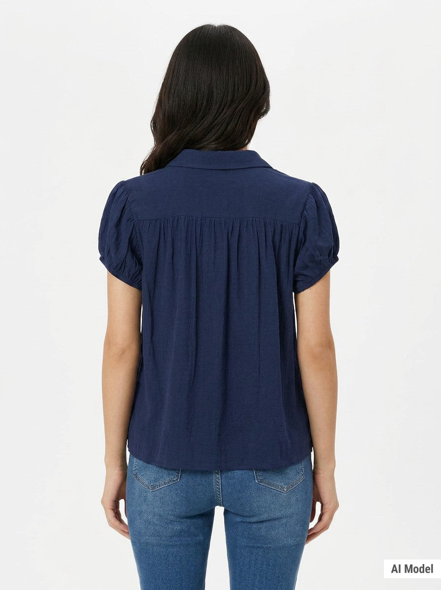 Woman's back view wearing a navy blue short puff-sleeve blouse with gathered yoke and collar, paired with blue jeans.
