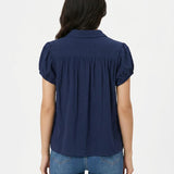 Woman's back view wearing a navy blue short puff-sleeve blouse with gathered yoke and collar, paired with blue jeans.