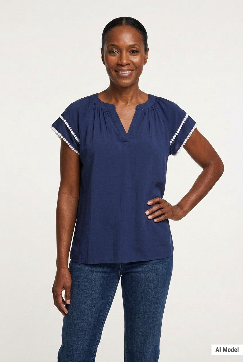 Navy blue gathered V-neck blouse with white pom-pom trim on flutter sleeves, worn by a woman, front view, waist-up.