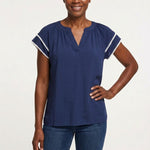 Navy blue gathered V-neck blouse with white pom-pom trim on flutter sleeves, worn by a woman, front view, waist-up.