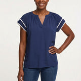 Navy blue gathered V-neck blouse with white pom-pom trim on flutter sleeves, worn by a woman, front view, waist-up.