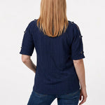 Back view of a woman with long blonde hair wearing a navy honeycomb-texture short-sleeve tunic with grommet details on