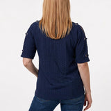 Back view of a woman with long blonde hair wearing a navy honeycomb-texture short-sleeve tunic with grommet details on