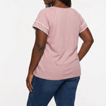 Plus-size woman with braids shown from the back wearing a dusty pink short-sleeve blouse with white lace trim on sleeves,