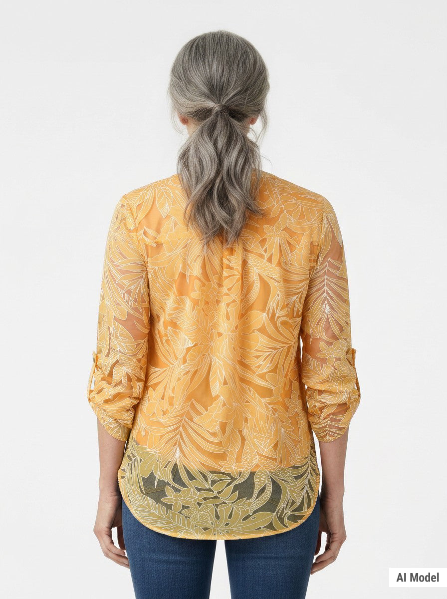 Back view of a woman with gray hair wearing an orange floral burnout blouse with rolled 3/4 sleeves and olive border hem,