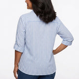 Back view of a woman wearing a blue and white vertical-stripe roll-tab 3/4-sleeve button-front blouse with dark jeans.