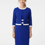 Older woman with gray hair models a sapphire blue 2-piece dress set with white trim at neckline, hem, and cuffs; front view,