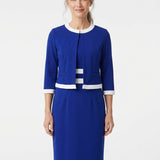 Older woman with gray hair models a sapphire blue 2-piece dress set with white trim at neckline, hem, and cuffs; front view,