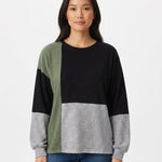 Woman wearing a color-blocked pullover in black, sage green, and heather gray with a crewneck and long sleeves; front view,