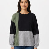 Woman wearing a color-blocked pullover in black, sage green, and heather gray with a crewneck and long sleeves; front view,