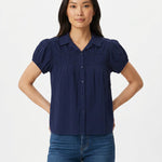 Woman wearing a navy blue short puff-sleeve button-front blouse with ruched yoke, lace trim details, and camp collar; front