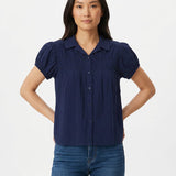 Woman wearing a navy blue short puff-sleeve button-front blouse with ruched yoke, lace trim details, and camp collar; front