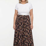 Black floral-print knit maxi skirt with sash waist tie, worn by a gray-haired woman with a white tee; full front view.