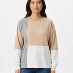 Woman wearing a colorblocked pullover with beige, white, and gray panels, crew neck, and long sleeves; front view, waist up.