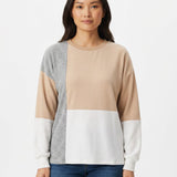 Woman wearing a colorblocked pullover with beige, white, and gray panels, crew neck, and long sleeves; front view, waist up.