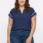 Navy blue split-neck popover blouse with white lace trim on flutter sleeves, worn by a plus-size woman with blue jeans,