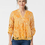 Woman with gray hair models a NY Collection orange tropical-print burnout blouse with V-neck and roll-tab sleeves, paired