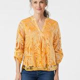 Woman with gray hair models a NY Collection orange tropical-print burnout blouse with V-neck and roll-tab sleeves, paired