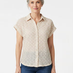 Front view of a woman wearing a beige floral lace button-front blouse with a collar and cuffed cap sleeves, paired with blue