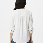 Back view of a woman wearing an ivory long-sleeve blouse with tab sleeves, back yoke pintuck detail, and a curved hem,