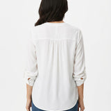 Back view of a woman wearing an ivory long-sleeve blouse with tab sleeves, back yoke pintuck detail, and a curved hem,