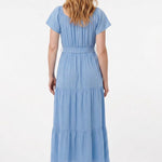 Light blue short-sleeve tiered maxi dress with waist tie belt, shown from the back on a woman with red wavy hair wearing