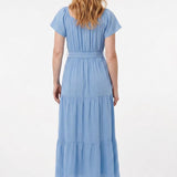 Light blue short-sleeve tiered maxi dress with waist tie belt, shown from the back on a woman with red wavy hair wearing