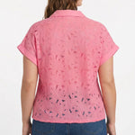Plus-size model wearing a pink short-sleeve eyelet button-front blouse with collar and cuffed sleeves, paired with dark