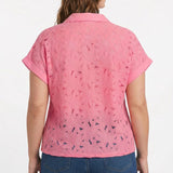 Plus-size model wearing a pink short-sleeve eyelet button-front blouse with collar and cuffed sleeves, paired with dark
