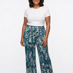 Teal floral wide-leg pull-on pants worn by a plus-size woman in her 60s, front view, paired with a white tee and nude heels.