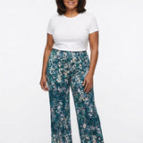 Teal floral wide-leg pull-on pants worn by a plus-size woman in her 60s, front view, paired with a white tee and nude heels.