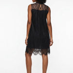 Woman wearing a black sleeveless lace shift dress with sheer high neck, scalloped hem, and keyhole back, shown from behind