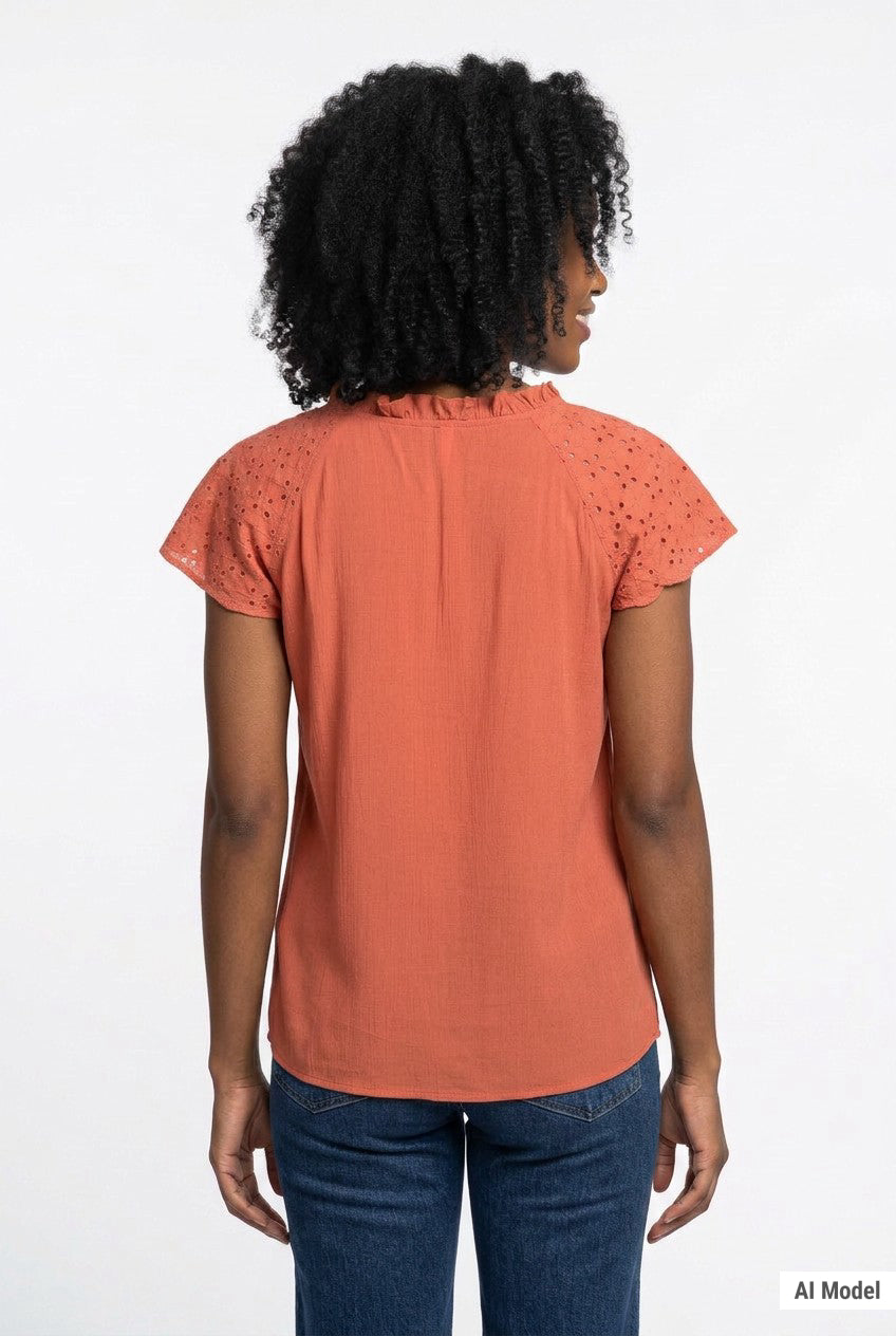 Woman wearing a rust-orange eyelet flutter-sleeve blouse with ruffle neckline, paired with dark jeans; back view.