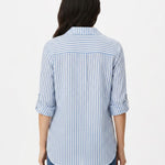 Back view of a woman wearing a blue and white vertical-stripe button-front blouse with rolled 3/4 sleeves and a back yoke,