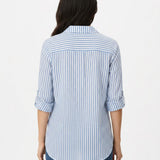Back view of a woman wearing a blue and white vertical-stripe button-front blouse with rolled 3/4 sleeves and a back yoke,