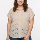 Plus-size woman wearing a beige short-sleeve eyelet button-front blouse with floral cutwork pattern; front view, waist up.